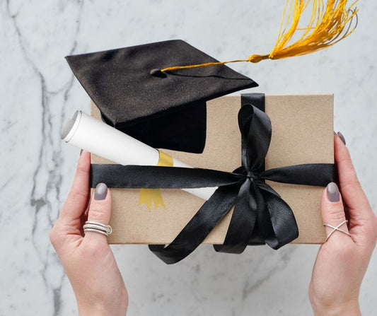 “Graduation surprise box with a journal, stationery, and celebratory treats next to a graduation cap.”