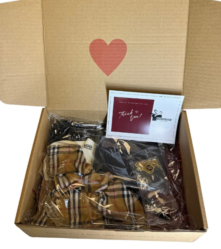 Open cardboard box with a heart design, containing wrapped items and a 'Thank you!' card. surpriseboxgift.com, gifts for women and men, 